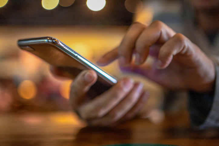 Closeup image of a man holding and using smart phone with coffee cup on wooden table in cafe Closeup image of a man holding and using smart phone with coffee cup on wooden table in cafe